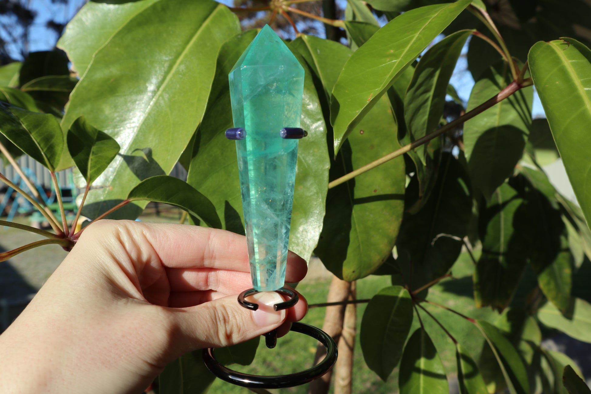 Hand holding a green crystal against a leafy background