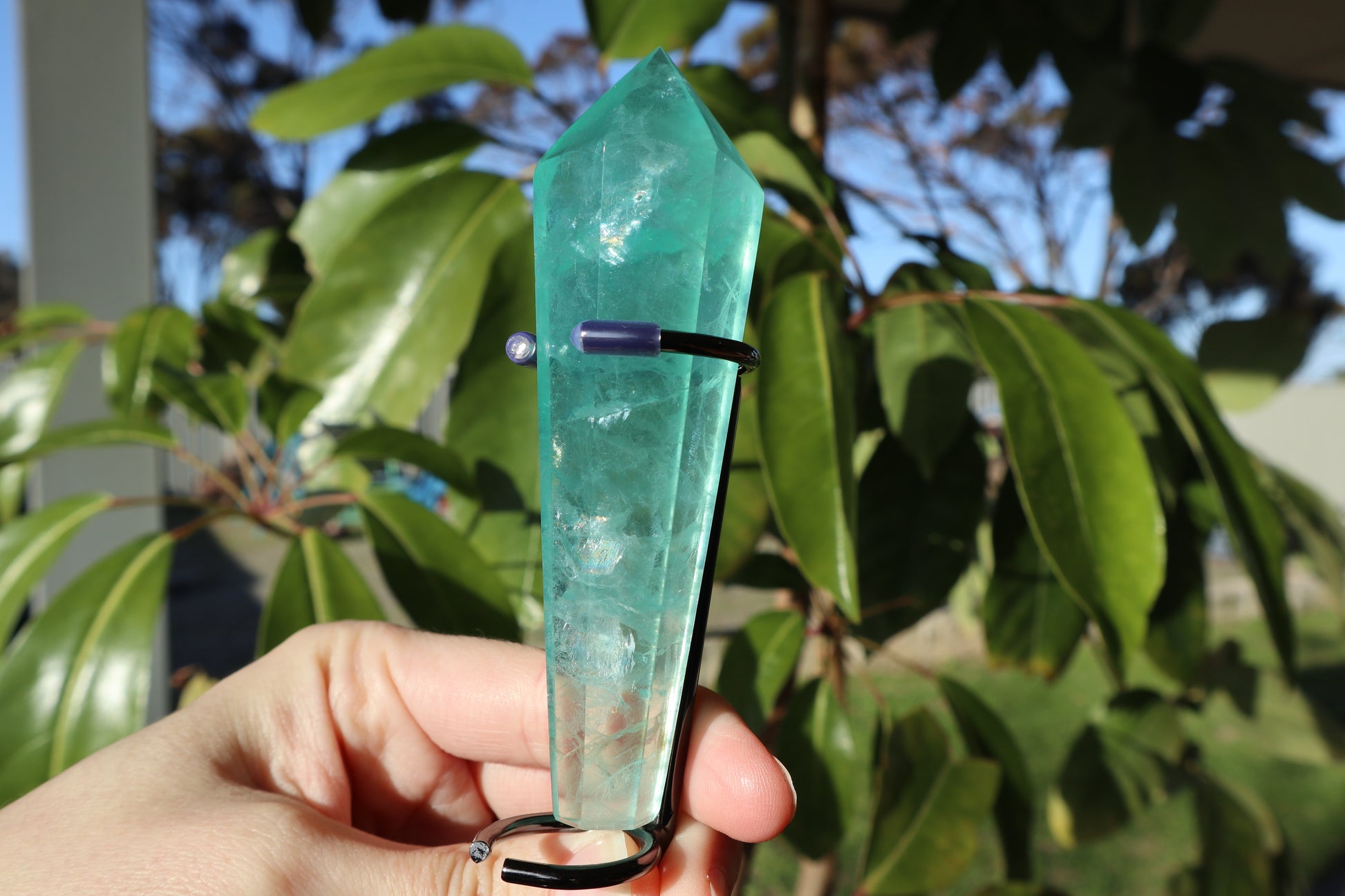 Green crystal object held by a hand with a leafy green background